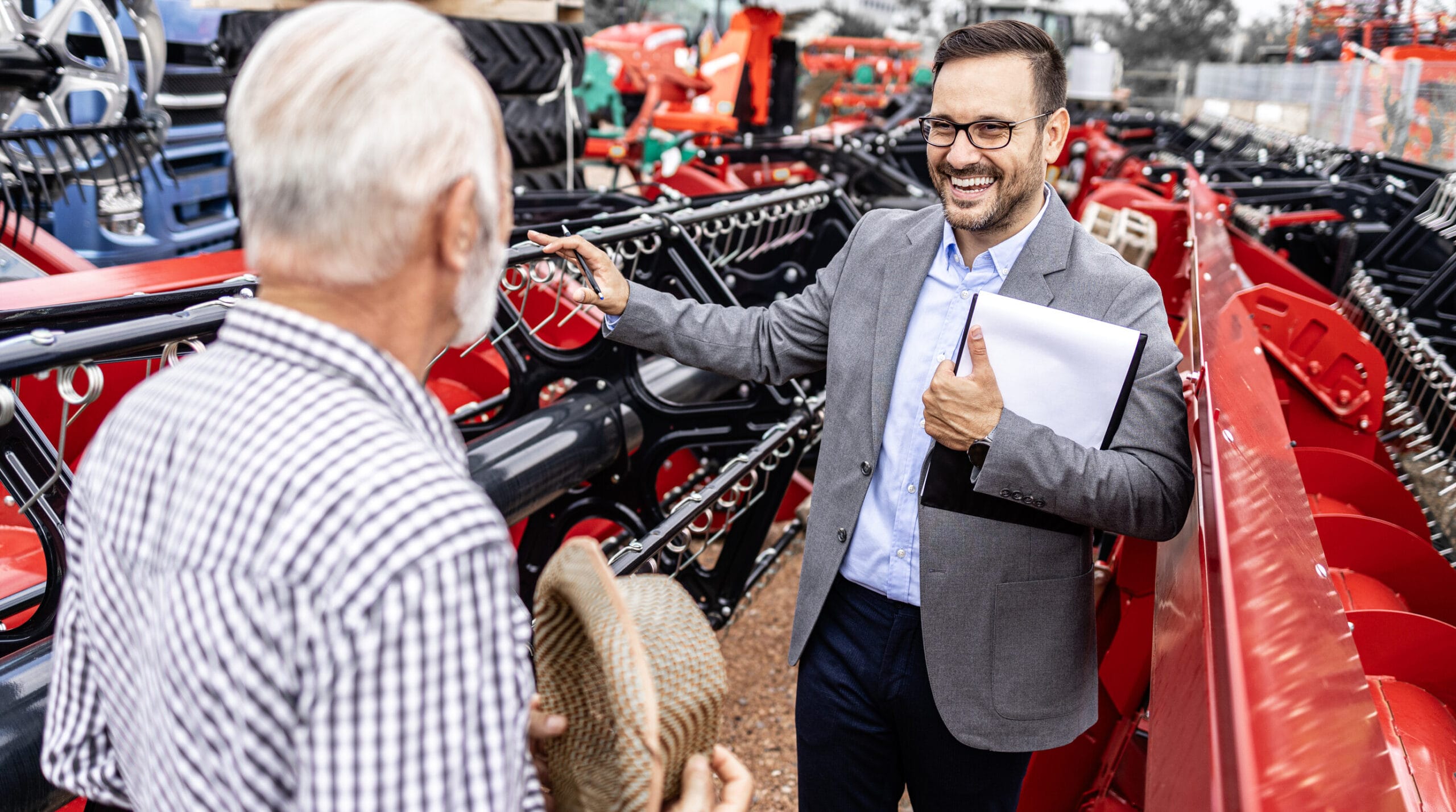 Profissional apresenta informações comerciais a um cliente ao lado de uma máquina agrícola